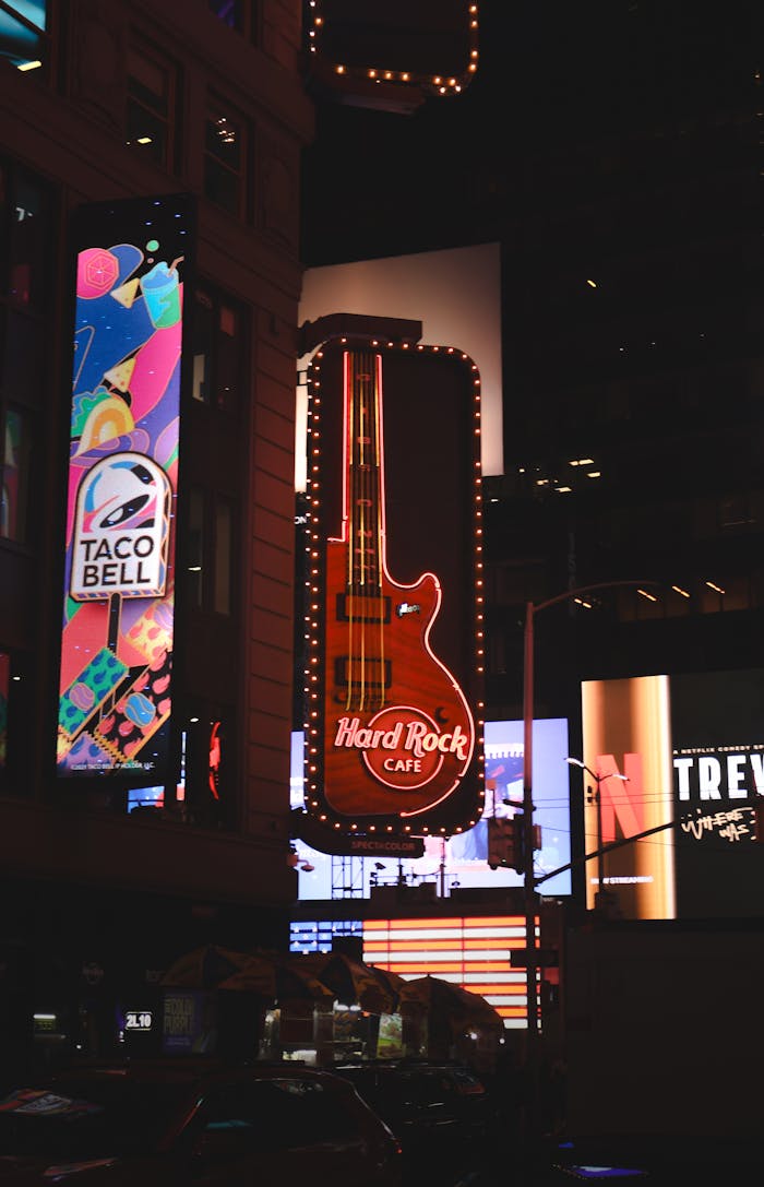 Vibrant neon signs illuminate Times Square at night featuring Hard Rock Cafe guitar.